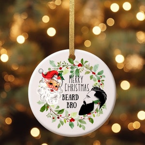 May include: White ceramic Christmas ornament with a green wreath, red berries, and the text "Merry Christmas Beard Bro". A cartoon Santa Claus and a man with a beard are inside the wreath.