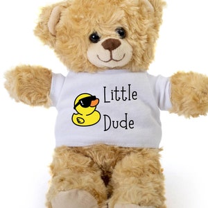 Puede incluir: Un oso de peluche beige que lleva una camiseta blanca con un pato de goma amarillo que lleva gafas de sol y el texto "Little Dude".