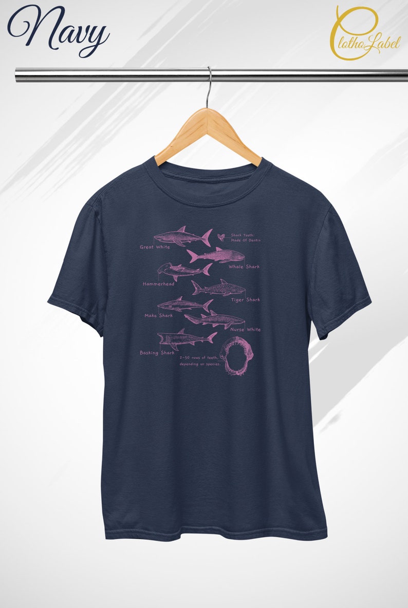 Pode incluir: Uma camiseta azul marinho com uma ilustra&ccedil;&atilde;o rosa de diferentes esp&eacute;cies de tubar&otilde;es, incluindo um grande tubar&atilde;o branco, um tubar&atilde;o martelo, um tubar&atilde;o tigre e um tubar&atilde;o baleia. O texto "Shark Teeth Made of Dentin" tamb&eacute;m est&aacute; inclu&iacute;do na camiseta.