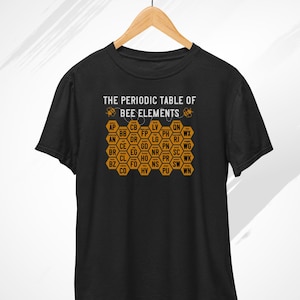 May include: Black t-shirt with a graphic of a periodic table of bee elements. The graphic is in a honeycomb pattern with the letters "BEE ELEMENTS" in white text above the table.