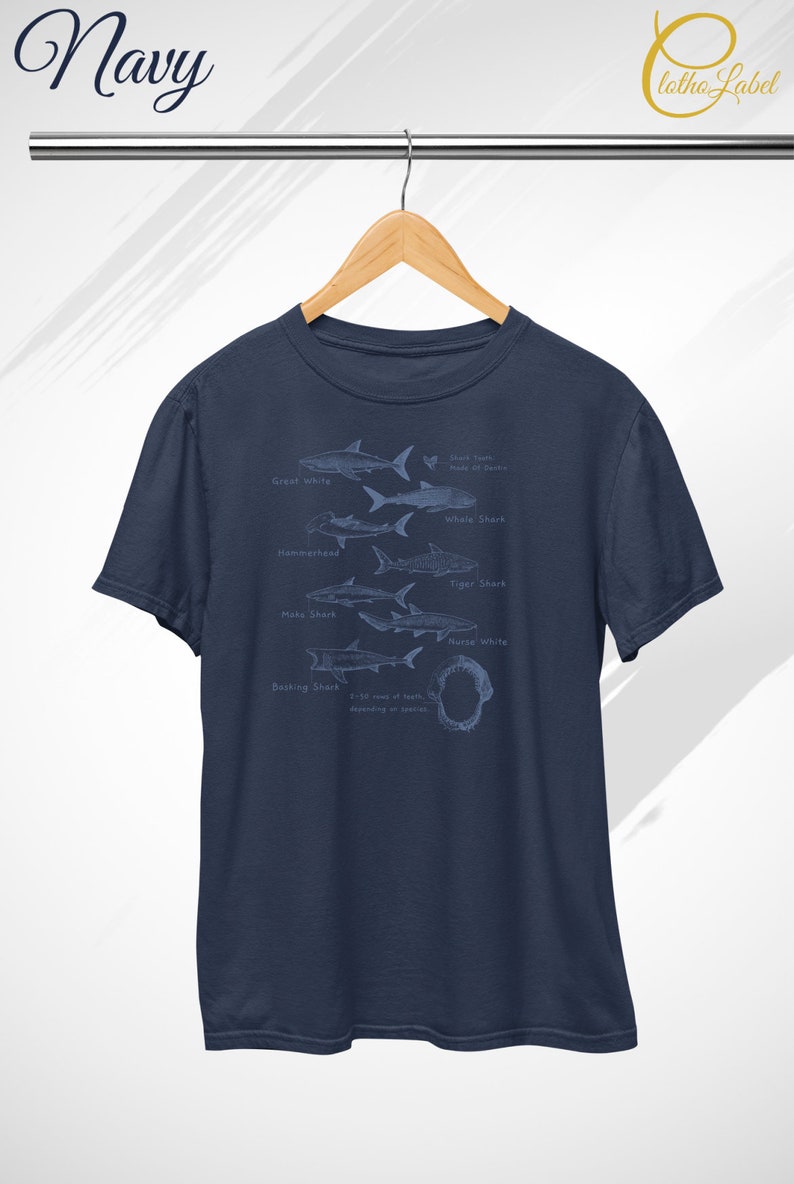 May include: A navy blue t-shirt with a graphic of different shark species, including the Great White, Whale Shark, Hammerhead, Tiger Shark, Mako Shark, Nurse Shark, and Basking Shark. The graphic also includes a shark tooth with the text "Shark Teeth Made of Dentine".
