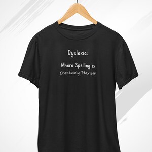 May include: Black t-shirt with white text that reads "Dyslexia: Where Spelling is Creatively Flexible"