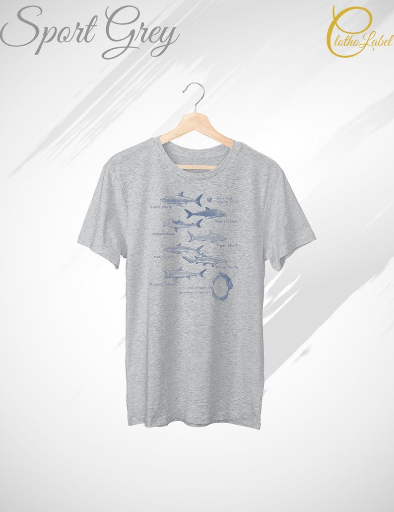 May include: A heather grey t-shirt with a graphic of different types of sharks, including the Great White, Whale Shark, Tiger Shark, Mako Shark, and Hammerhead Shark. The text "Shark Teeth" is printed above the graphic, and the text "Respect the Ocean" is printed below the graphic.