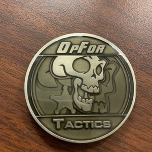 May include: A silver-colored coin with a skull and crossbones design. The coin has the words "OpFor Tactics" inscribed on it.