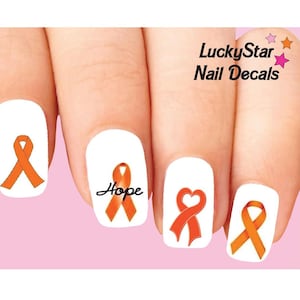 May include: Nail art decals with orange awareness ribbons on white nail polish. One nail features the word "Hope" in black script. The LuckyStar Nail Decals logo is in the upper right. The background is light pink.