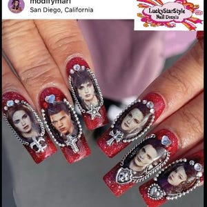 May include: Red glitter nail art featuring portraits of characters from a movie, framed with silver chains and embellishments. Each nail showcases a different character, with various charms and gems. The nails are long and almond-shaped.