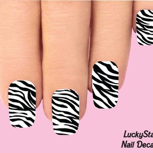Puede incluir: Calcomanías de uñas con estampado de cebra en blanco y negro. Las calcomanías tienen forma rectangular curva y están aplicadas en uñas. El fondo es de color rosa claro. El texto "LuckyStar Nail Decals" es visible en la esquina inferior derecha.