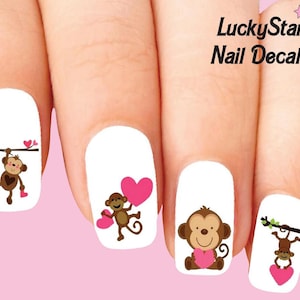 Könnte beinhalten: Nagelaufkleber mit Cartoon-Affen, die rosa Herzen halten. Die Affen sind braun mit hellbraunen Gesichtern und werden in verschiedenen Posen dargestellt. Der Text "LuckyStar Nail Decals" ist sichtbar.