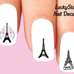 Puede incluir: Calcomanías de uñas con diseños de la Torre Eiffel en negro. Un diseño incluye espirales decorativas rosas y negras. El texto "LuckyStar Nail Decals" es visible. Fondo rosa claro.