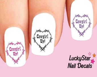 Può includere: Decalcomanie per unghie bianche con una forma a cuore formata da filo spinato con il testo Cowgirl Up! all'interno. Le decalcomanie sono applicate su tre unghie. Il testo LuckyStar Nail Decals e tre piccole stelle sono stampati nell'angolo.