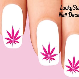 Könnte beinhalten: Weiße Nagelaufkleber mit einem leuchtend pinkfarbenen Cannabisblatt-Design. Das Bild enthält den Text "LuckyStar Nail Decals" in Schwarz. Die Aufkleber werden auf einem rosa Hintergrund gezeigt.