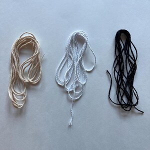 May include: Three spools of twine in different colors: natural, white, and black. The twine is wound into a loose coil.