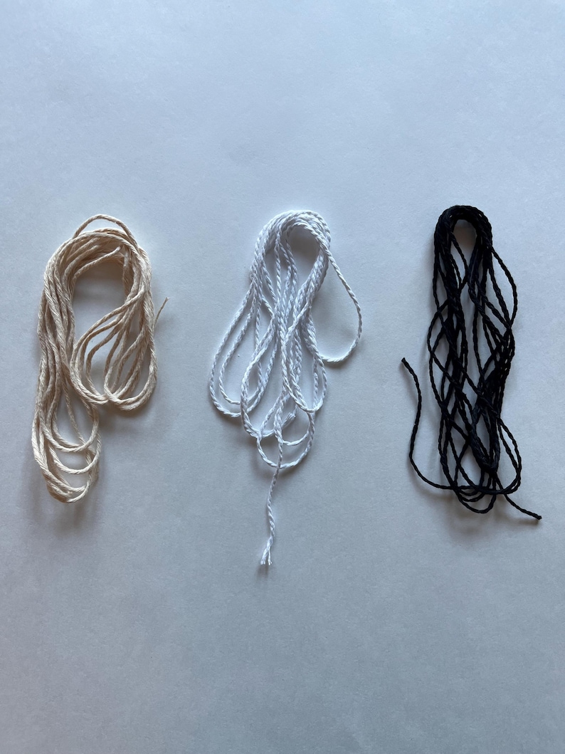 May include: Three spools of twine in different colors: natural, white, and black. The twine is wound into a loose coil.