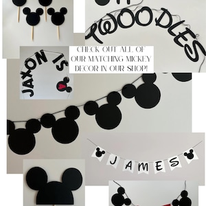 Puede incluir: Una colecci&oacute;n de decoraciones para fiestas con el tema de Mickey Mouse en negro. Incluye adornos para cupcakes, pancartas con nombres y la palabra "ONE", y un letrero que dice "JAXON IS". Tambi&eacute;n es visible el texto "CHECK OUT ALL OF OUR MATCHING MICKEY DECOR IN OUR SHOP!"
