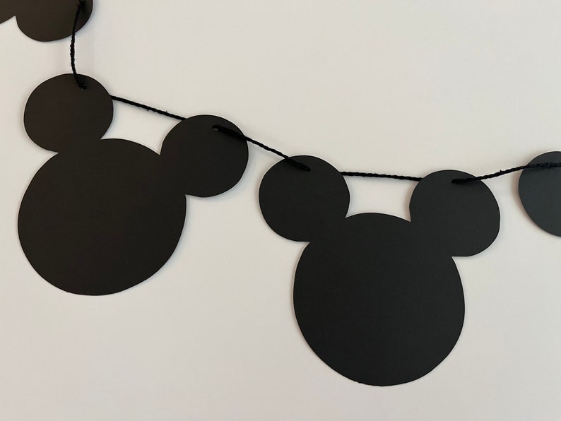 Puede incluir: Guirnalda de papel con tem&aacute;tica de Mickey Mouse en blanco y negro con cuerda negra. La guirnalda est&aacute; hecha de recortes de papel de cabezas de Mickey Mouse.