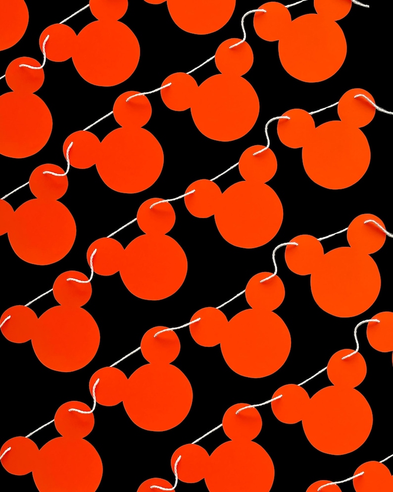 May include: A string of orange Mickey Mouse head cutouts on a black background. The cutouts are connected by white string.