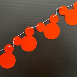 May include: A red and white string banner with four Mickey Mouse head cutouts. The banner is strung together with white string.