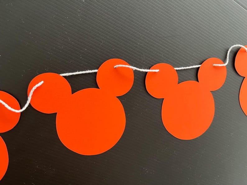 May include: A red and white Mickey Mouse themed banner with red paper cutouts of Mickey Mouse heads strung together with white string.
