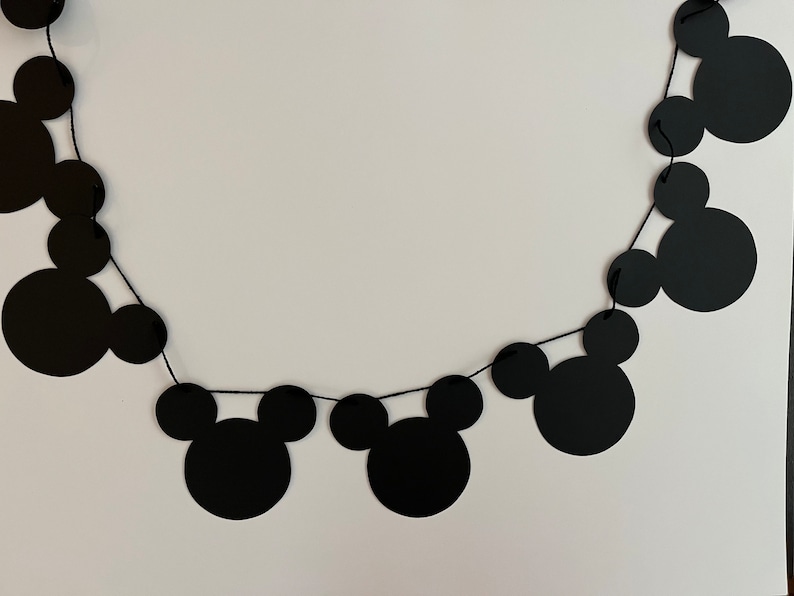 Puede incluir: Guirnalda de papel con tem&aacute;tica de Mickey Mouse en blanco y negro con cuerda negra. La guirnalda est&aacute; hecha de recortes de papel de cabezas de Mickey Mouse.