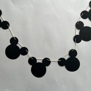 May include: Black and white Mickey Mouse themed party banner with black paper cutouts of Mickey Mouse heads strung on white string.