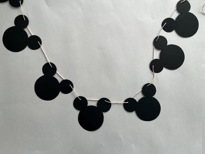 May include: Black and white Mickey Mouse themed party banner with black paper cutouts of Mickey Mouse heads strung on white string.