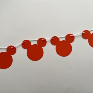 May include: Red paper Mickey Mouse head cutouts strung together with white string to create a party banner.