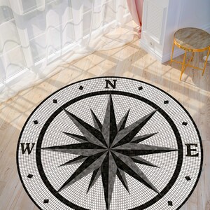 Pode incluir: Um tapete de b&uacute;ssola redondo com um design de mosaico em preto e branco. A b&uacute;ssola aponta para norte, sul, leste e oeste. O tapete &eacute; redondo e tem uma borda preta.