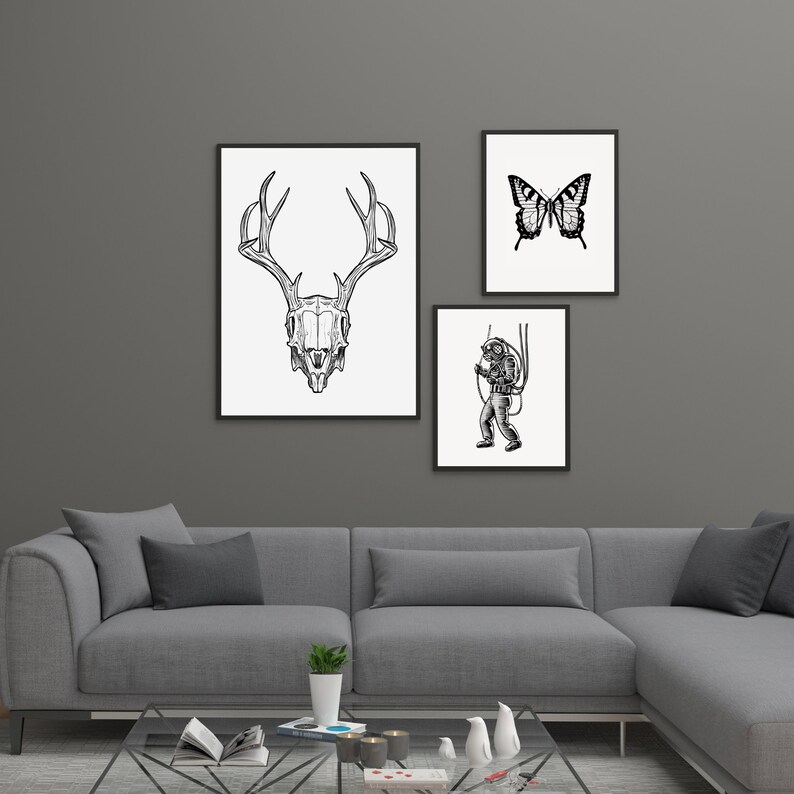 Peut inclure: Trois impressions d'art encadr&eacute;es sur un mur gris. Les impressions pr&eacute;sentent un cr&acirc;ne de cerf en noir et blanc, un papillon et un plongeur. Les impressions sont dans des cadres noirs et sont accroch&eacute;es au-dessus d'un canap&eacute; sectionnel gris.