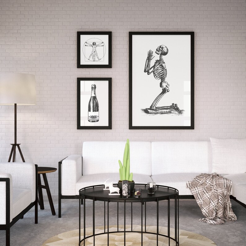 Peut inclure: Trois impressions d'art encadr&eacute;es en noir et blanc sont accroch&eacute;es au-dessus d'un canap&eacute; blanc. Les impressions repr&eacute;sentent un squelette, une bouteille et un dessin de l'Homme de Vitruve. Une table basse en m&eacute;tal noir avec un cactus et des objets d&eacute;coratifs est devant le canap&eacute;.