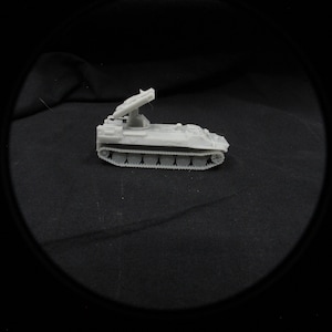Könnte beinhalten: Ein kleines, hellgraues Modell eines Militärfahrzeugs mit Raketenwerfer. Das Fahrzeug hat eine Kettenbasis und einen erhöhten Werfer. Das Modell ist vor einem dunklen Hintergrund platziert.