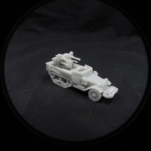 May include: A gray plastic model of a military half-track vehicle with a mounted gun turret. The model is detailed with tracks, wheels, and a driver's compartment.