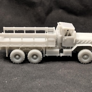 May include: A white plastic model of a military truck with a flatbed and a cab. The truck has four wheels and a raised bed with sides.