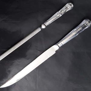 Op de afbeelding: Twee zilveren bestekdelen, een is een mes met een puntige punt en de andere is een vijl met een afgeronde punt. Beide hebben sierlijke handvatten met bloemmotieven.