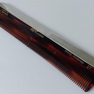 May include: A Kent of London hair comb featuring a tortoiseshell-patterned body with a metallic silver-toned spine. The text reads MADE IN GT. BRITAIN, KENT OF LONDON, HAND FINISHED, and 2T. The comb has fine teeth along one edge.
