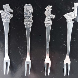 Peut inclure: Quatre fourchettes à apéritif argentées avec des manches détaillées. Chaque fourchette présente un design différent : un aigle, une figure avec le mot "PERU", une personne avec un chapeau et un oiseau. Les fourchettes sont présentées sur un fond sombre.