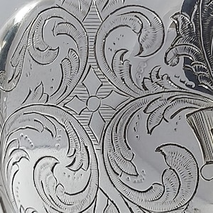 Puede incluir: Primer plano de una tetera de plata con un intrincado diseño floral grabado.