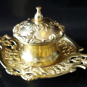 Op de afbeelding: Een gouden messing inktpot met een decoratief deksel en een bijpassend dienblad. Het deksel heeft het jaar "1919" gegraveerd.