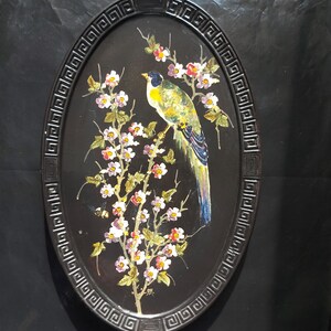 May include: An oval-shaped black tray with a decorative border. The tray features a hand-painted design of a yellow and blue bird perched on a branch with white flowers.