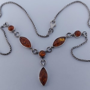 May include: A silver necklace featuring a delicate chain and five amber stones. The design includes two marquise-shaped amber pieces, two round amber stones, and a central marquise-shaped amber pendant drop, all set in polished silver metal links.