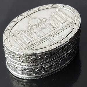Puede incluir: Caja de alhajas ovalada de plata con un diseño en relieve del Taj Mahal en la tapa. La caja tiene un borde decorativo alrededor del borde.