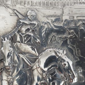 May include: A detailed, silver-toned relief sculpture depicting a historical scene. The artwork features figures on horseback, with one figure raising an arm. The relief also includes architectural elements and additional figures, all rendered in fine detail.