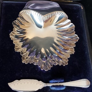 May include: A silver heart-shaped dish with a scalloped edge, and a matching silver butter knife, both in a black velvet lined box.