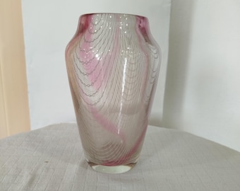 May include: A clear glass vase with a pink and white swirled design. The vase has a wide base and tapers upwards, with a slightly flared rim. The pink design is layered over a white background, creating a textured effect.