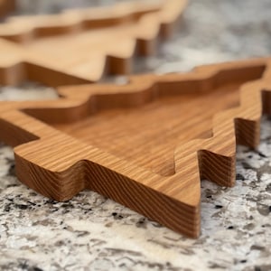 May include: Wooden Christmas tree-shaped trays. The trays are made of light brown wood and have a carved-out interior. The edges of the trays are slightly rounded. The trays are designed to resemble a Christmas tree.