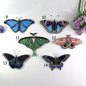 May include: A collection of six colorful butterfly ornaments. The butterflies feature various designs and colors, including blue, green, pink, and black. Each butterfly has a unique pattern and is made of a translucent material.