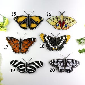 May include: A collection of six decorative butterfly ornaments. Each butterfly features intricate designs with various color schemes, including yellow, orange, black, and white. The wings are outlined in black, and each butterfly has a unique pattern.