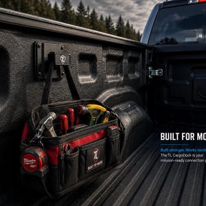 May include: Black truck bed with a mounted black bracket holding a red and black tool bag. The bag contains various tools, including a hammer, screwdrivers, and a tape measure. Text on the bag reads "BUILT TO WORK". The text "BUILT FOR MORE" is also visible.