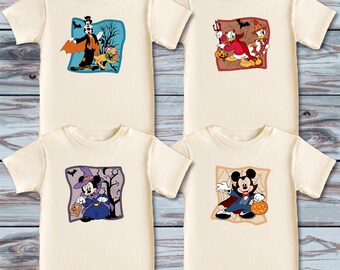 May include: Four cream-colored t-shirts with Halloween-themed cartoon character designs. Each shirt features a different character: a vampire, Donald Duck, Minnie Mouse as a witch, and Mickey Mouse as a vampire, all holding pumpkins.