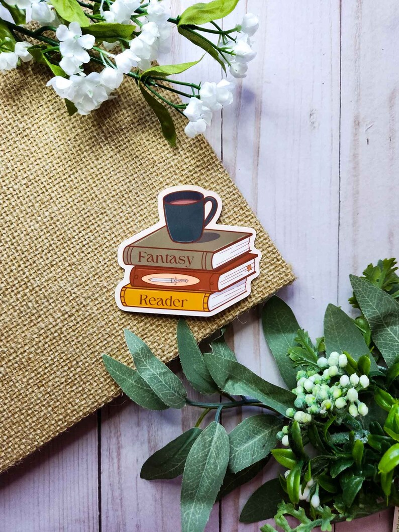 May include: A sticker with a stack of three books, a cup of coffee on top, and the words "Fantasy Reader". The sticker is on a brown burlap background.