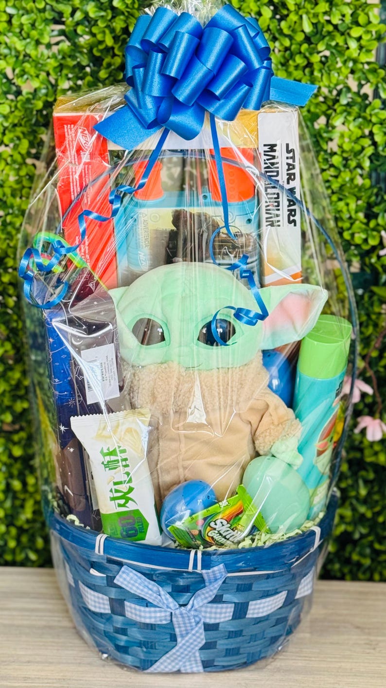 Pu&ograve; includere: Un cesto regalo blu pieno di vari articoli, tra cui un peluche di Grogu, un libro di Star Wars Mandalorian e snack. Il cesto &egrave; avvolto in cellophane trasparente e legato con un grande fiocco blu. Contiene anche prodotti per il bagno e caramelle.